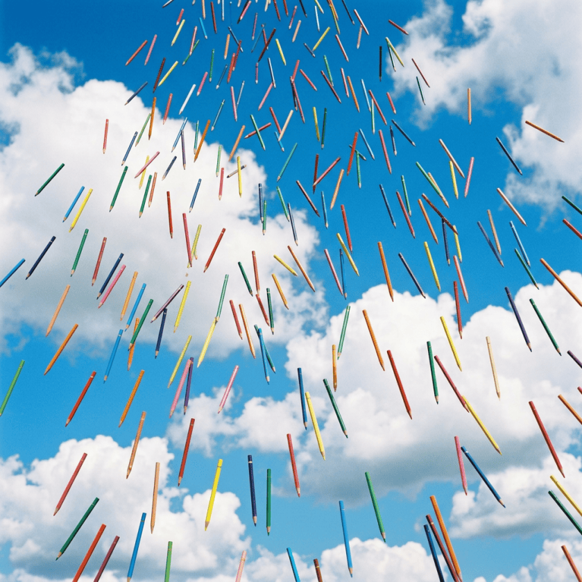 Colorful pencils falling against a blue sky with white clouds